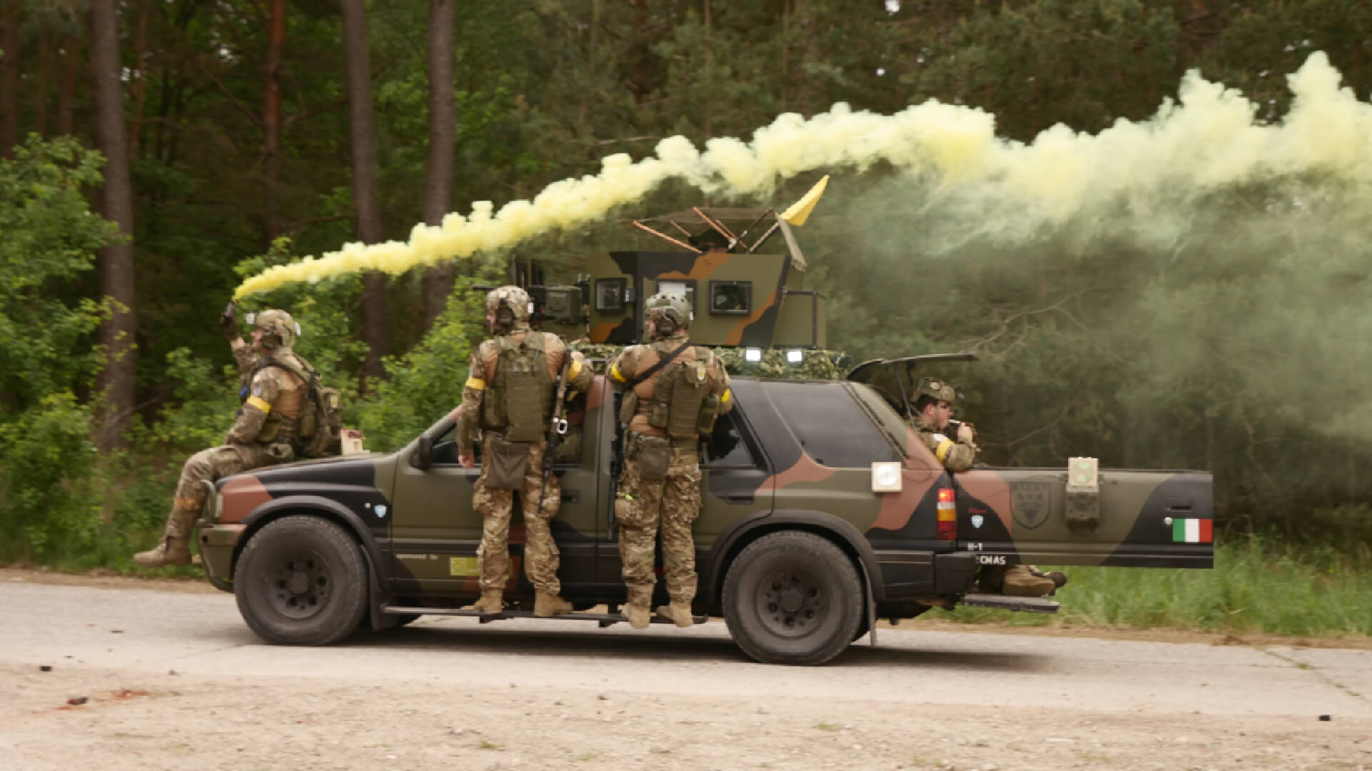 Airsoft-Spieler in Tarnkleidung auf einem Fahrzeug mit gelbem Rauch im Wald.