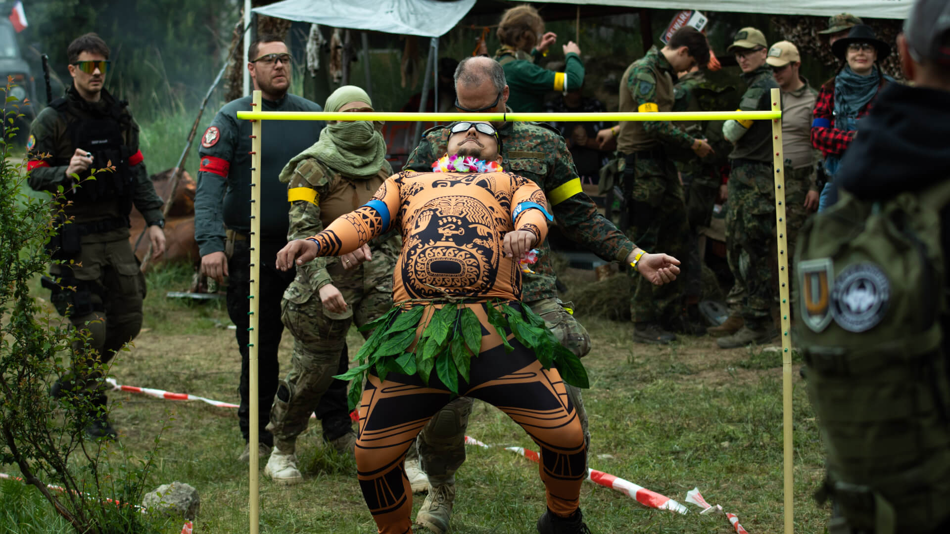 Airsoft-Event: Teilnehmer in Kostümen beim Limbo-Wettbewerb auf einem Feld mit Zuschauern.