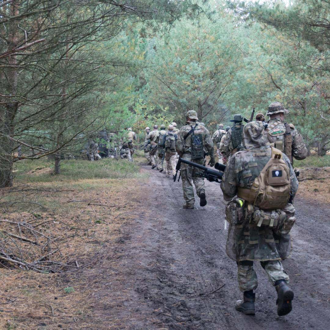 Airsoft-Team in Tarnkleidung marschiert durch bewaldeten Weg.