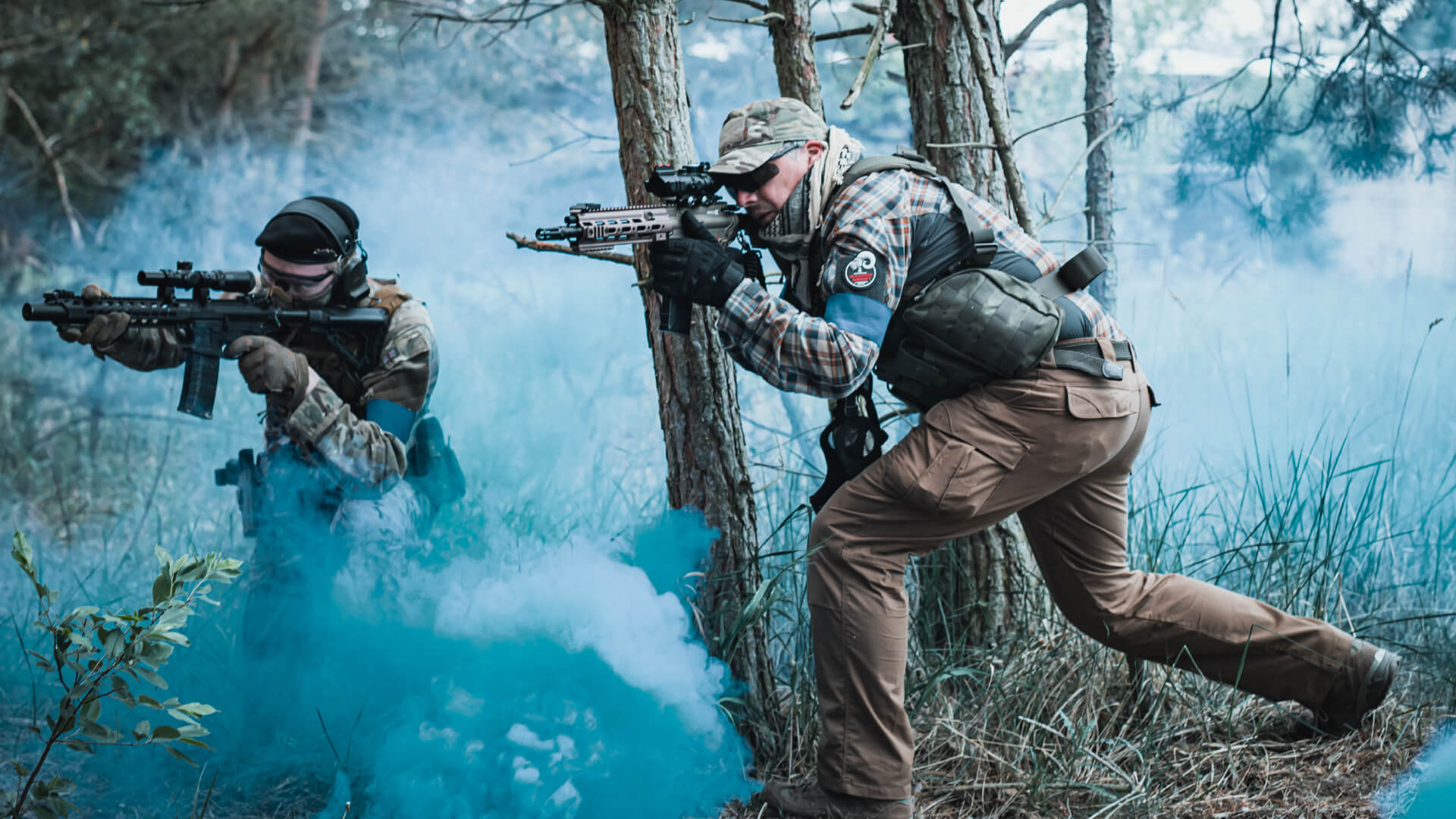 Zwei Airsoft-Spieler im Wald mit Rauch in Deckung und Zielposition.