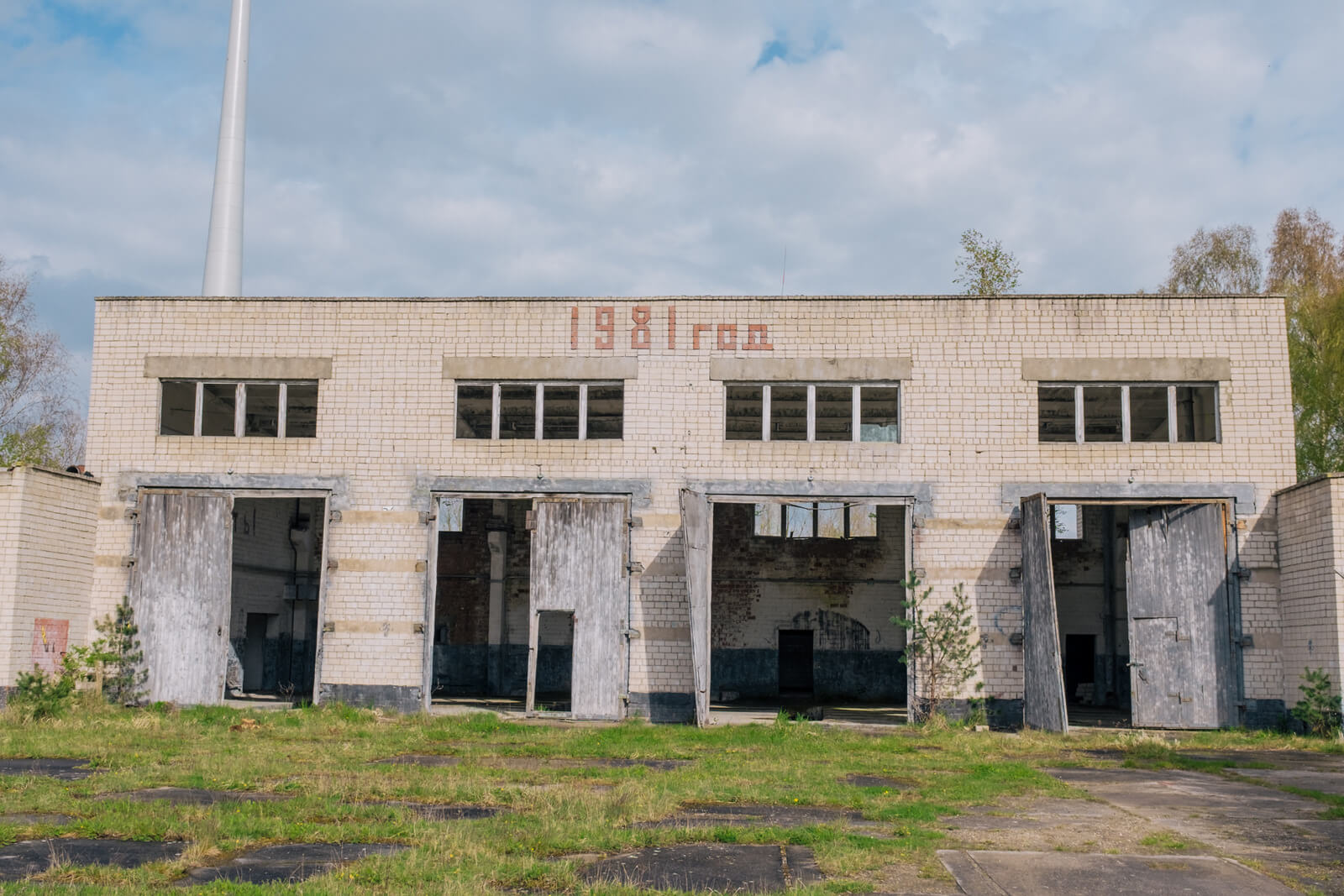 Verlassene Backsteingebäude mit offener Fassade und bewachsenem Gelände, geeignet für Airsoft-Spiele.