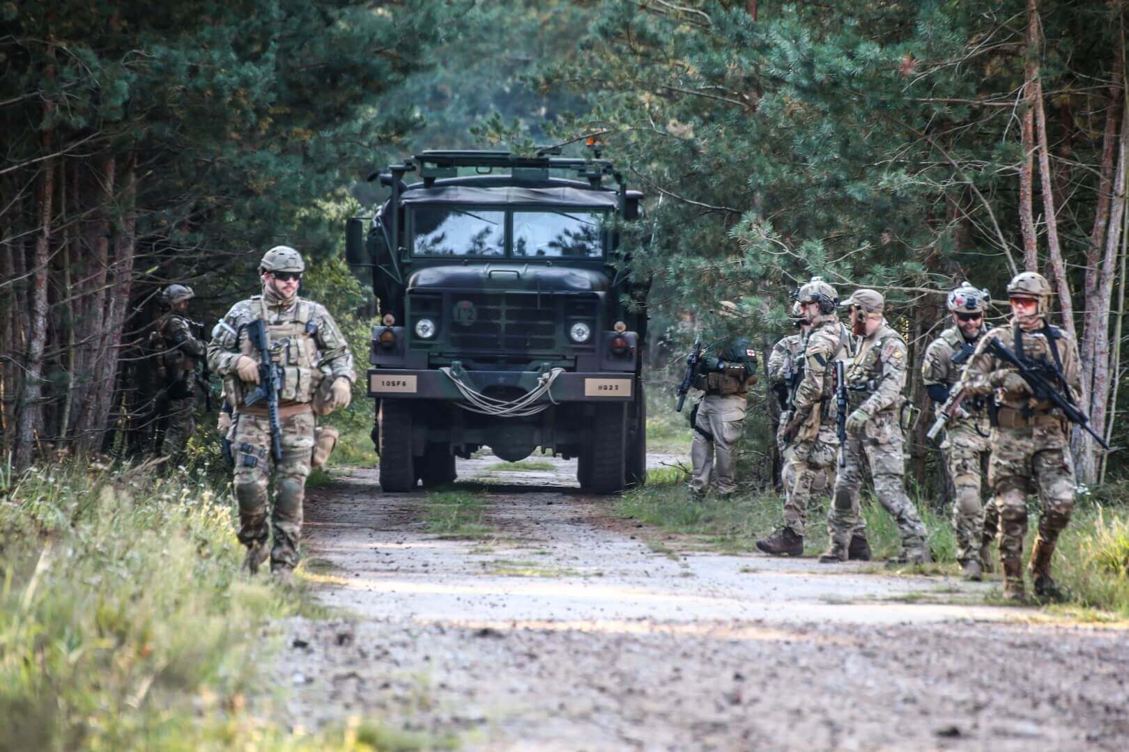 Airsoft-Team in militärischen Uniformen marschiert auf Waldweg vor einem großen Fahrzeug.