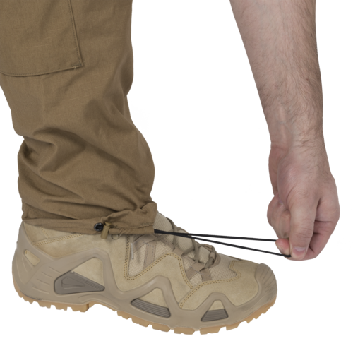 MBDU® Trousers - NyCo Ripstop - MultiCam Black™ Person zieht elastische Kordel an einer braunen Hose über beigem Wanderschuh fest.