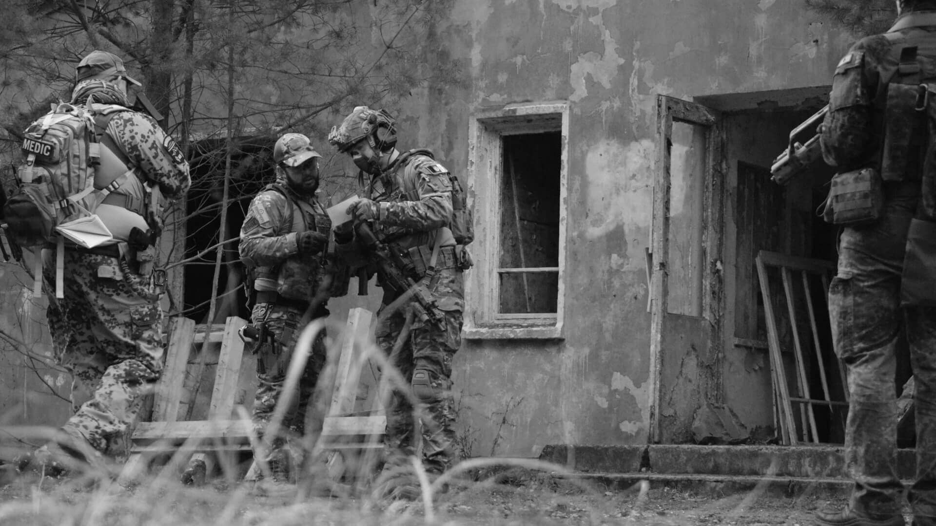 Airsoft-Team in Tarnkleidung vor einem verfallenen Gebäude, Diskussion über Strategie.