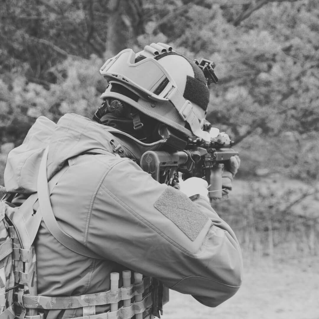 Airsoft-Spieler mit Helm, taktischer Ausrüstung und Gewehr im Freien.