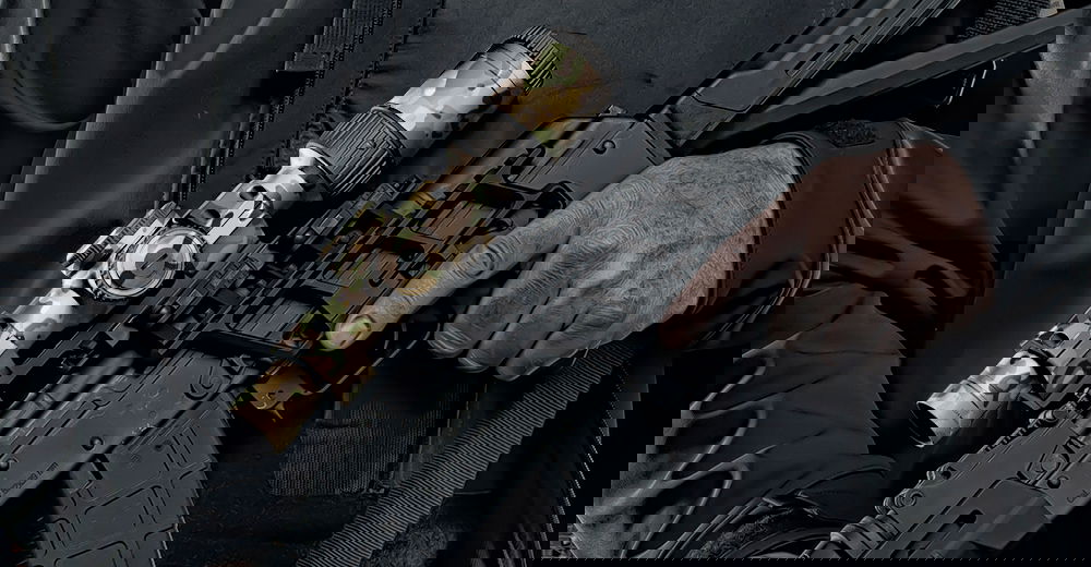 Person mit Gewehr in Tarnoptik und Zielfernrohr hält den Abzug fest.